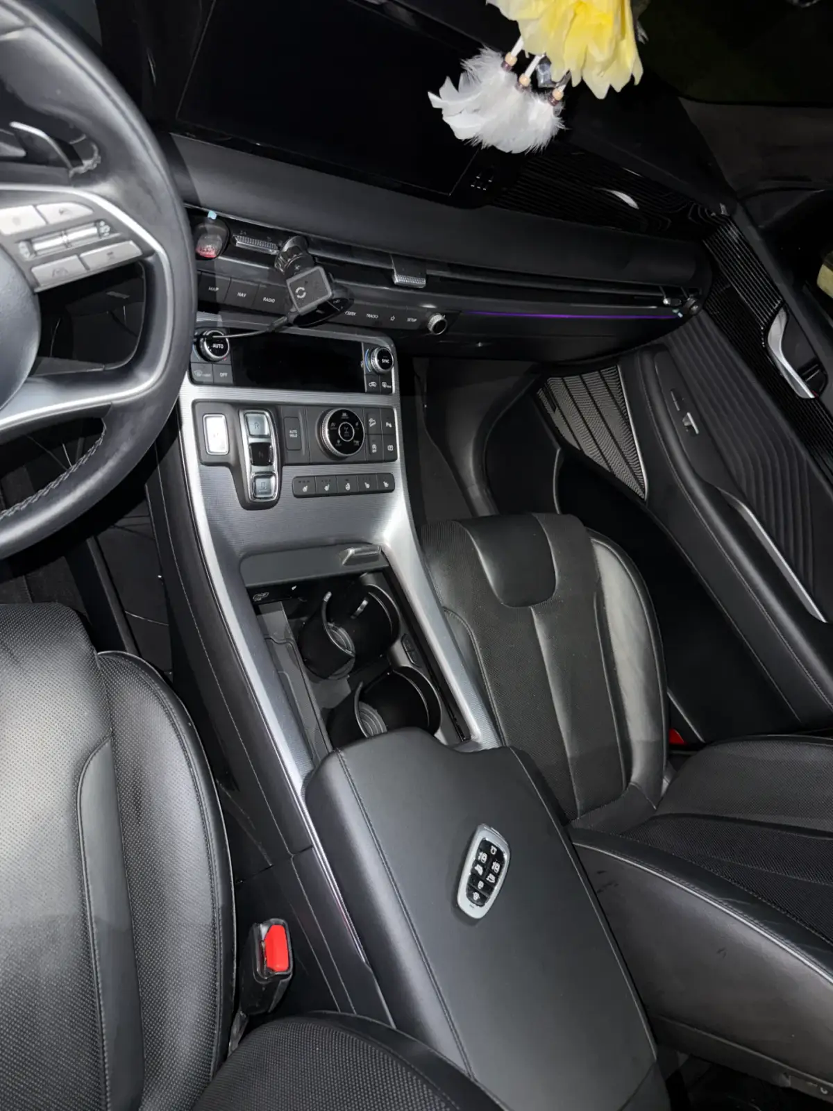 Car interior with black seats, a silver-trimmed center console, cup holders, dashboard controls, and a partially visible steering wheel.
